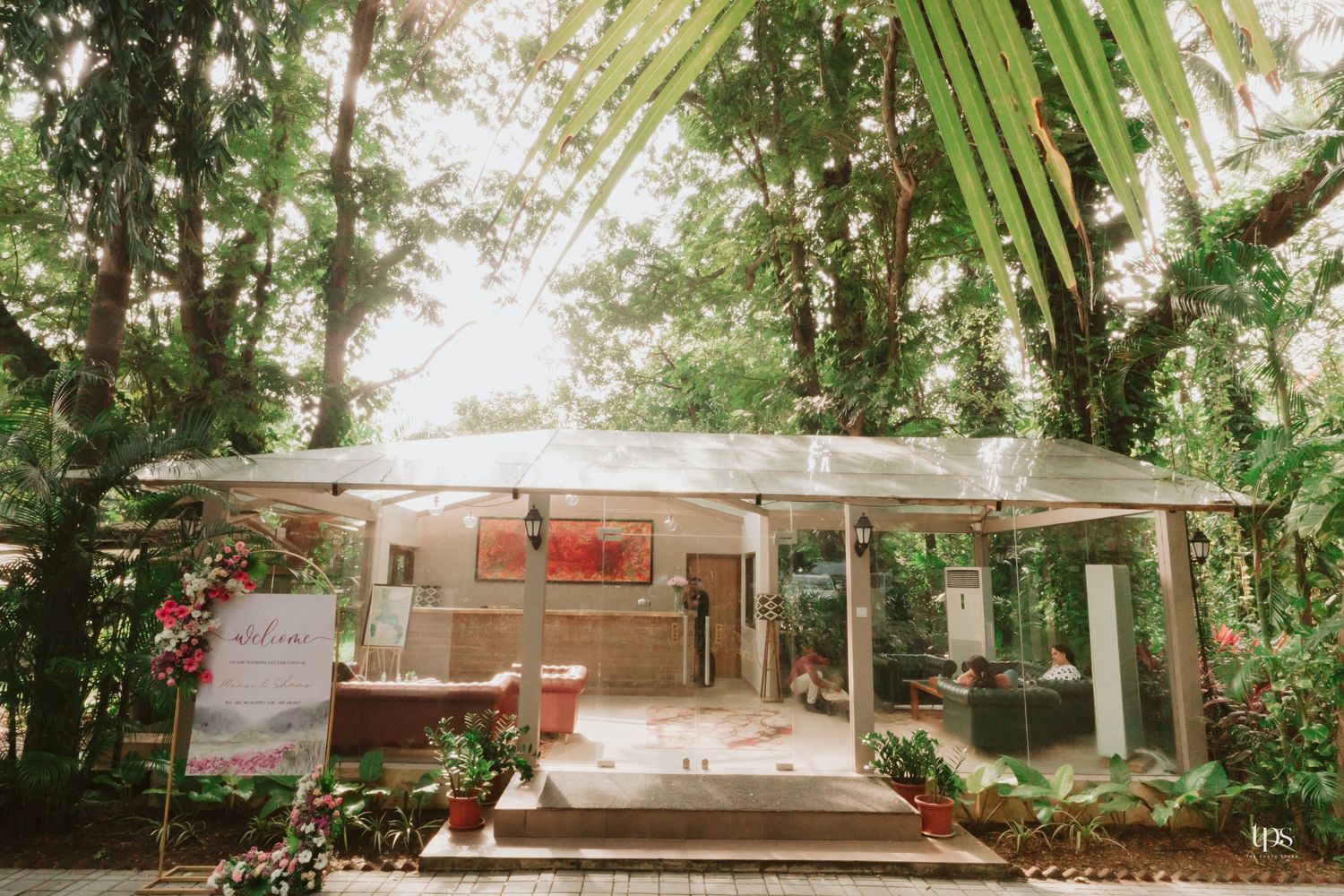 Outdoor venue pathway lined with tropical plants and palm trees under natural sunlight.