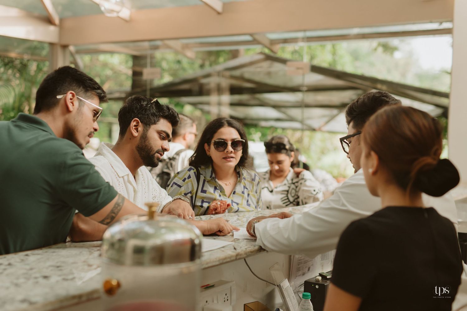 People mingling at outdoor tables under a covered patio surrounded by tropical landscaping.