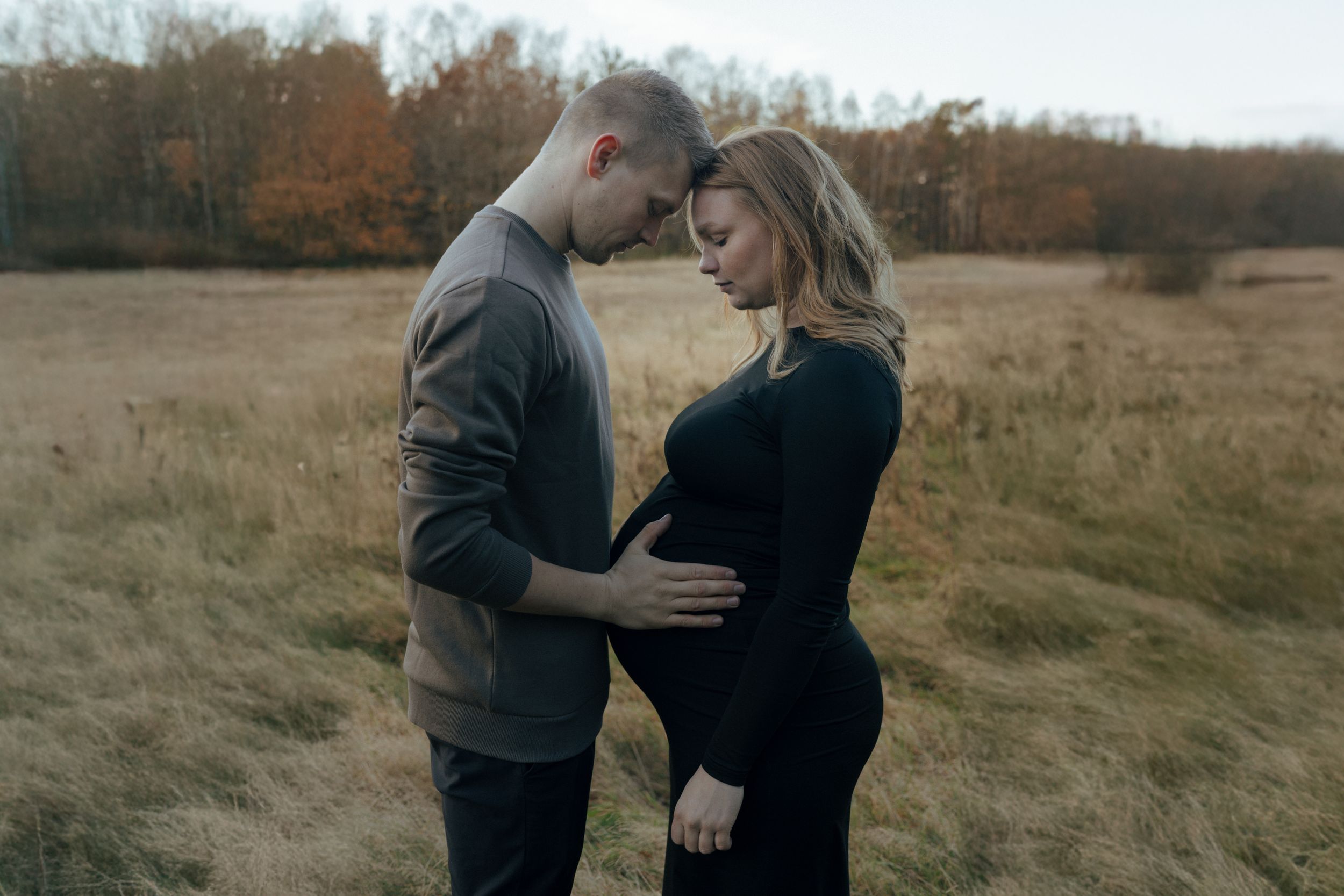 A tender maternity photoshoot moment captured outdoors in a golden autumn field at sunset.