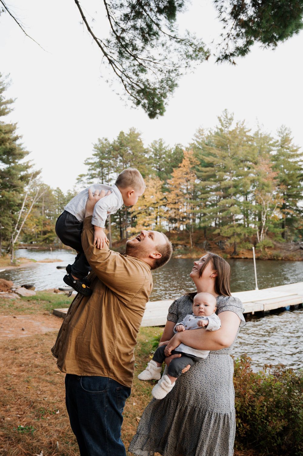 Family enjoying autumn day by lake with parents playing with small children in scenic forest setting.