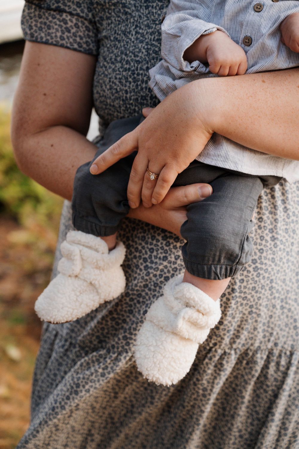 Close-up of tiny feet in white booties resting on someone wearing a gray patterned dress.