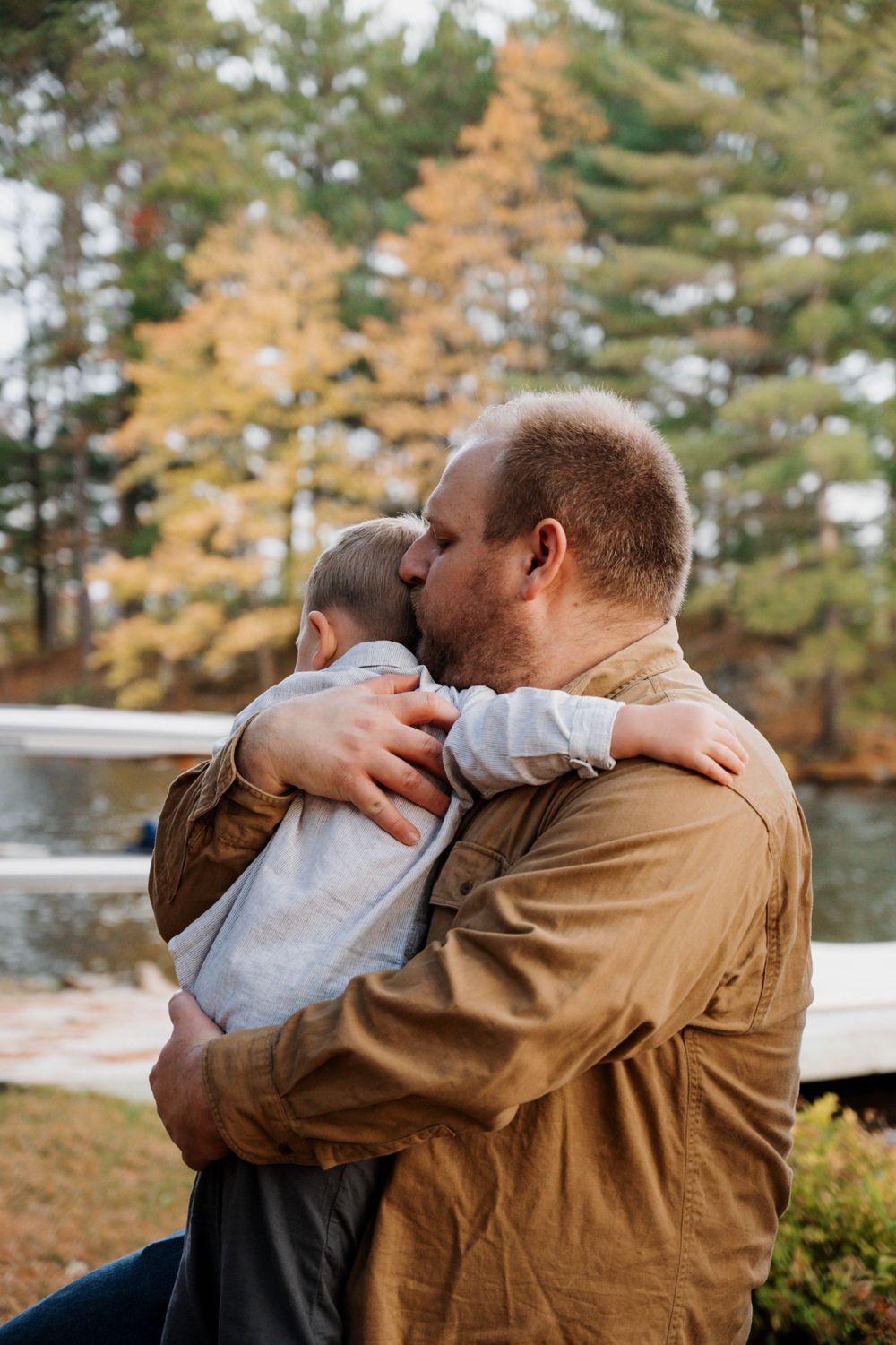 An intimate outdoor autumn moment shared by parent and child near a lake surrounded by pine trees.