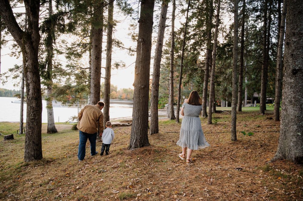 Family walking together through wooded trail near lake on autumn day.