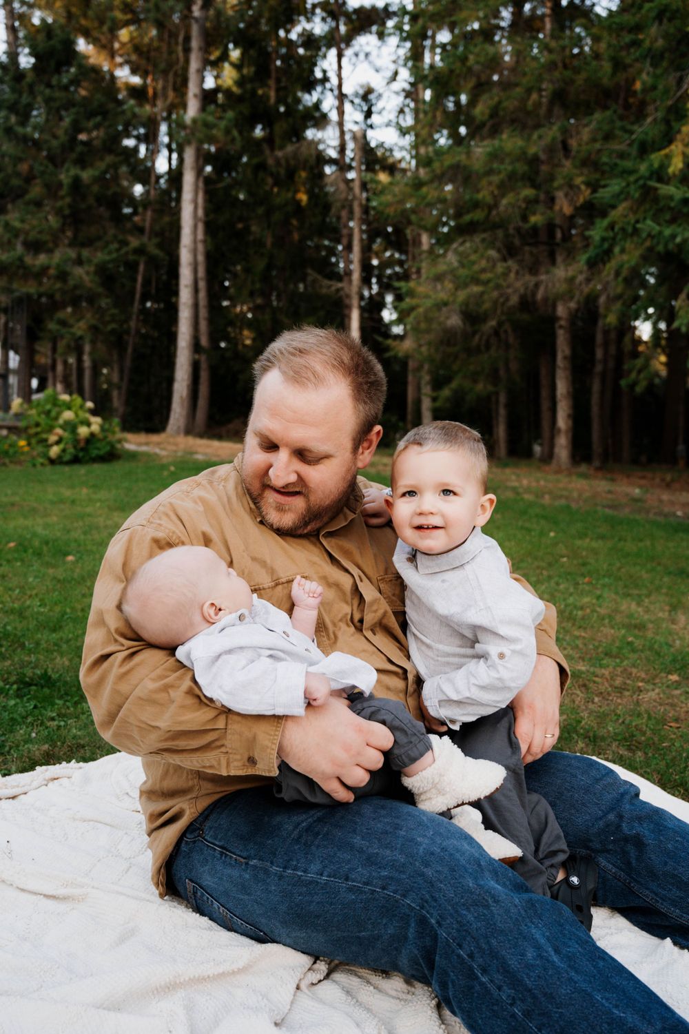 A loving moment on a blanket in a wooded backyard setting during a family photo session.