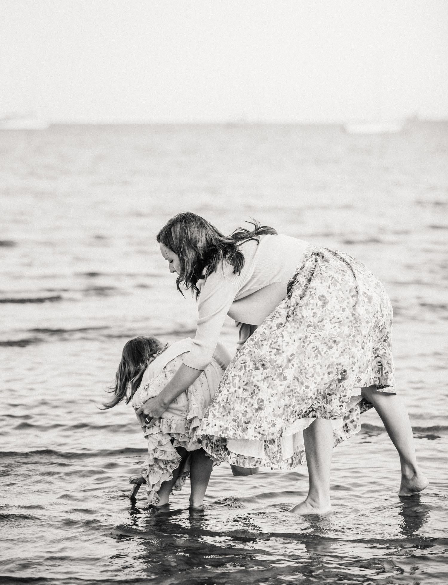 Mother and daughter paddling in the sea on a beach in Dorset, Weymouth. They are hugging candidly. The image is a black and white photograph