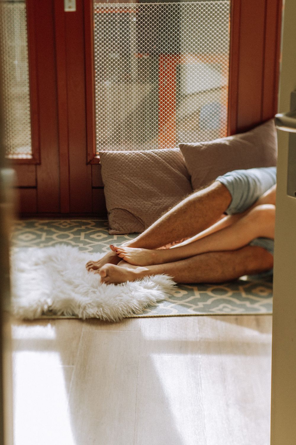 Close-up of bare feet resting on white fluffy rug near window.