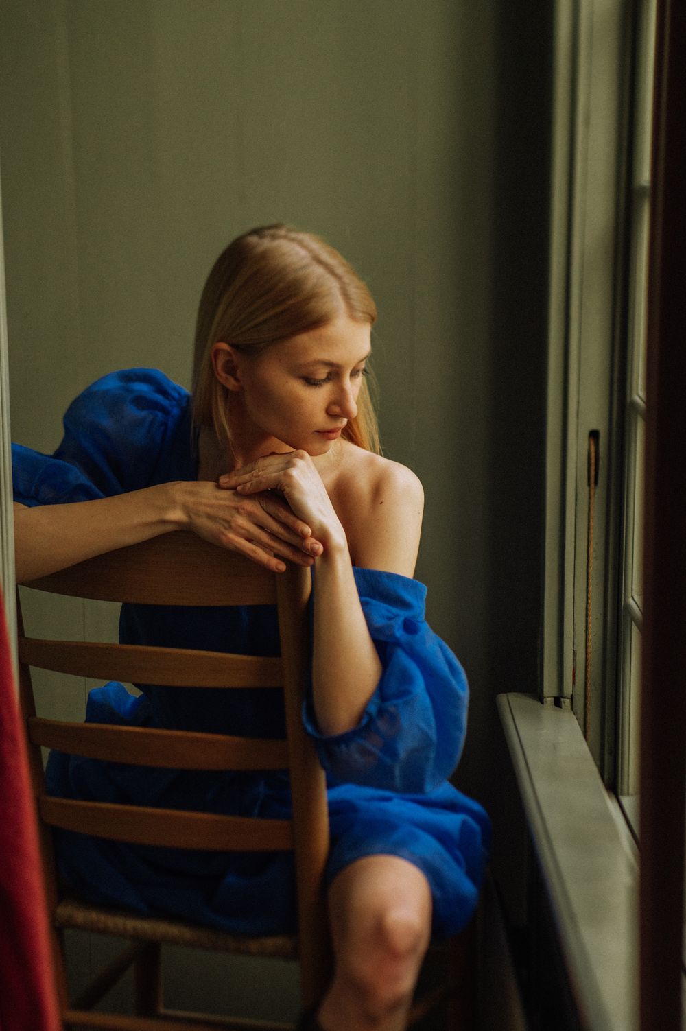 Moody sequence showing someone in a blue outfit resting their head on a wooden chair.