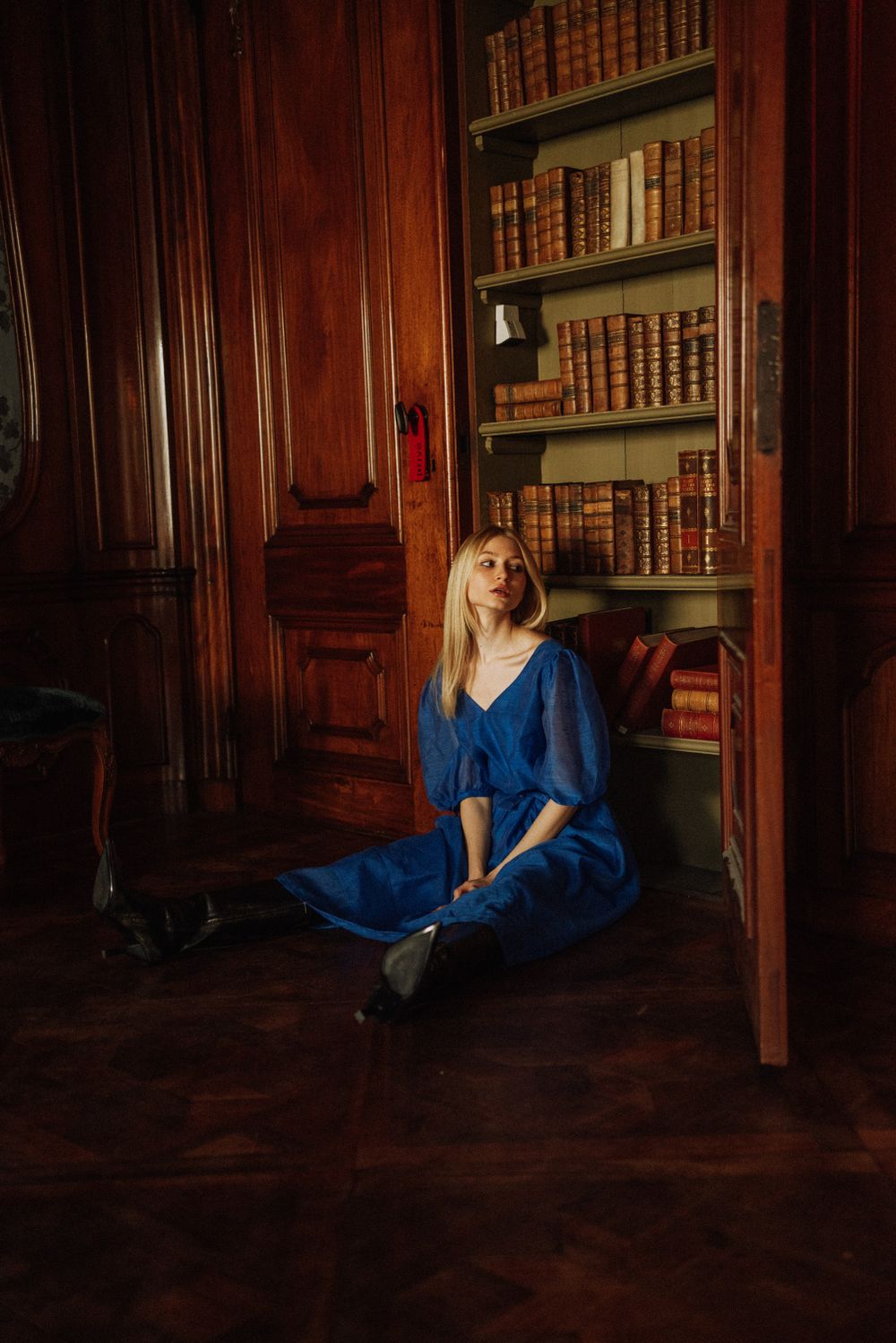 Artistic shots of someone in blue dress sitting on floor of library with wood paneling.