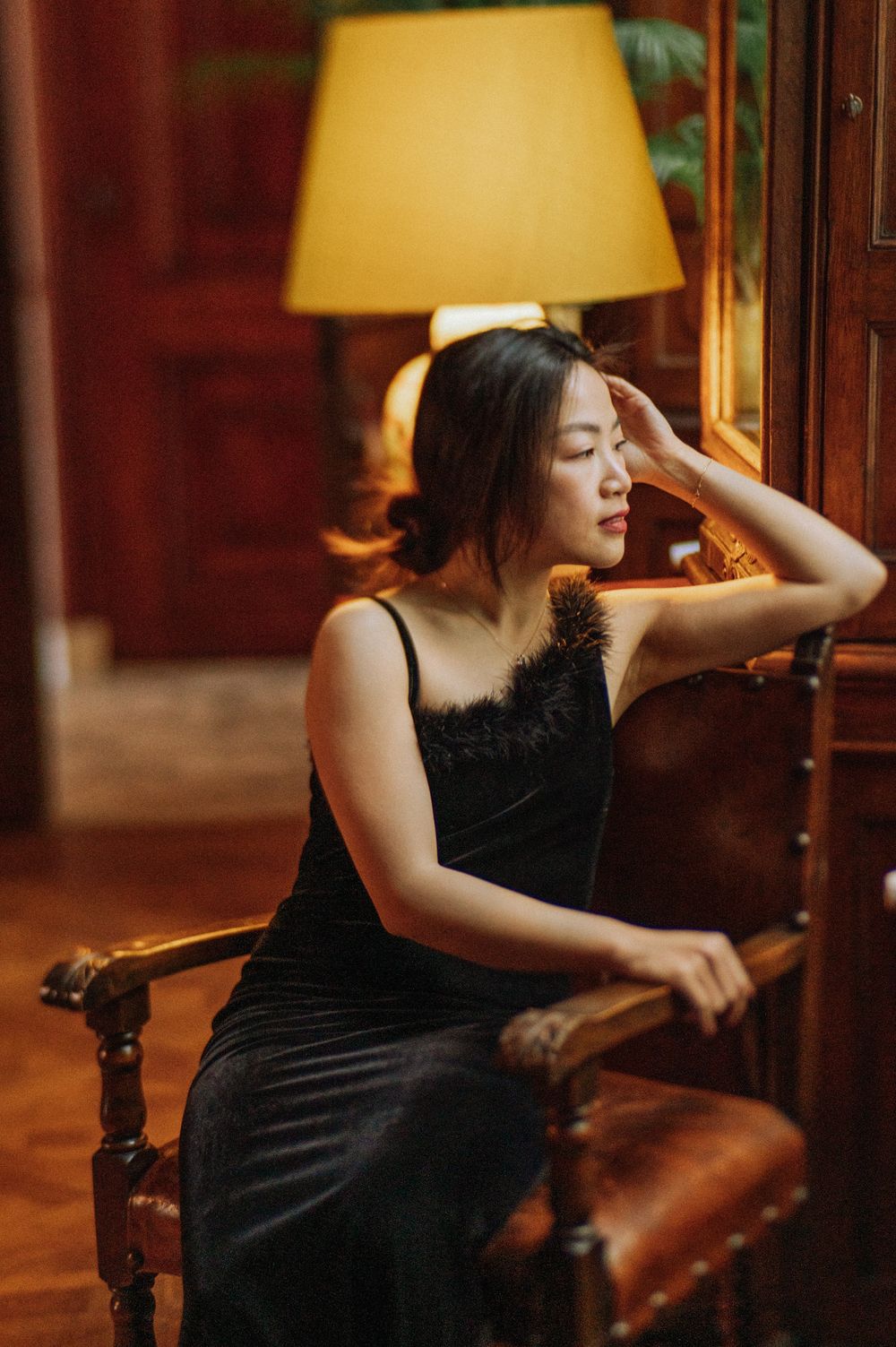 Dramatic portraits in a dimly lit room with a warm lamp glow and elegant black dress.