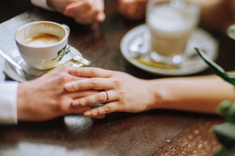 Coffee cups and hands reaching across wooden table in intimate cafe setting.