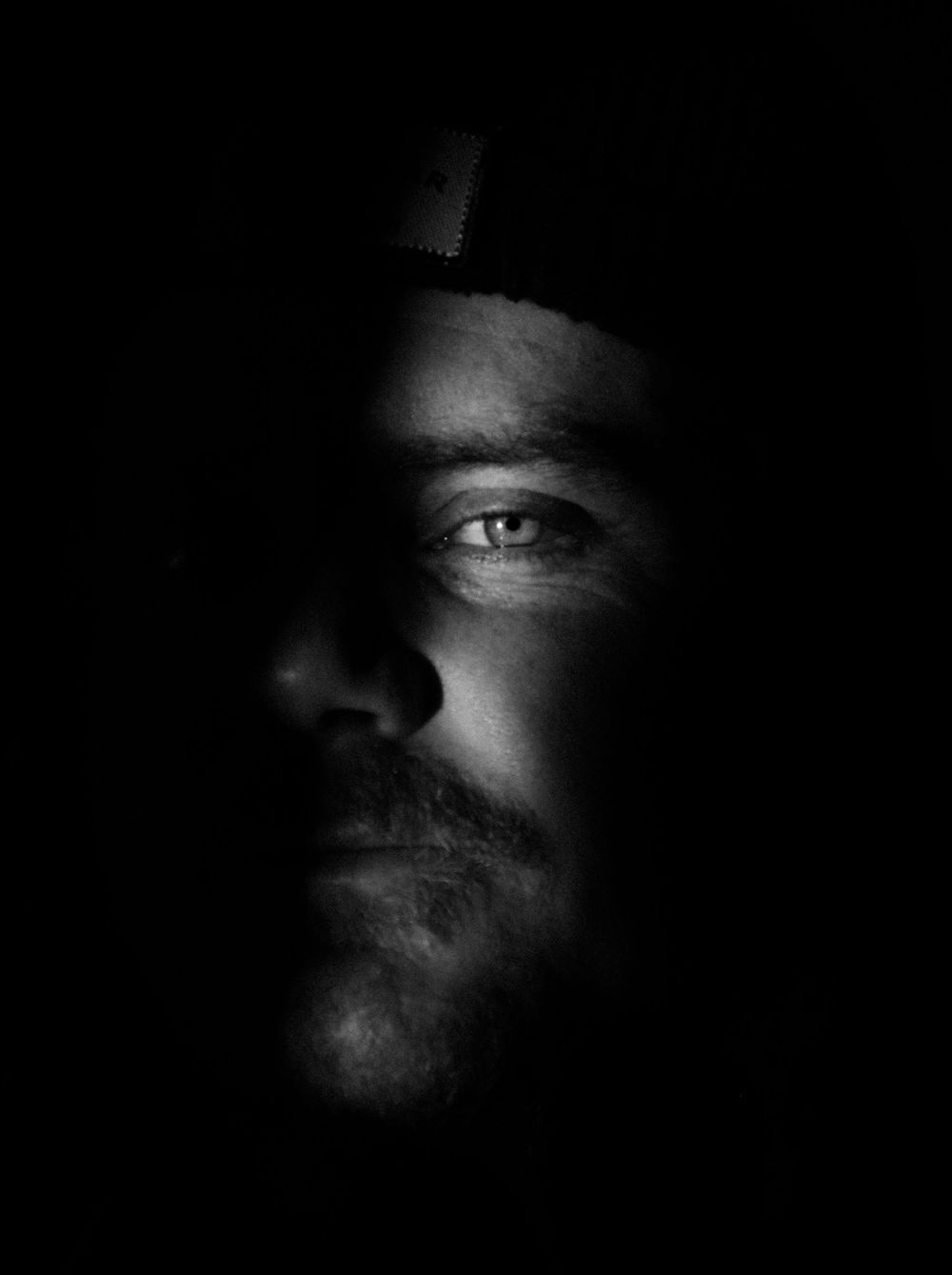 Dramatic black and white close-up portrait showing half a face emerging from darkness.
