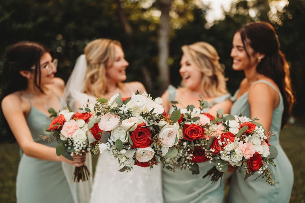 Bridesmaids in mint green dresses hold stunning red and white bouquets while laughing together.