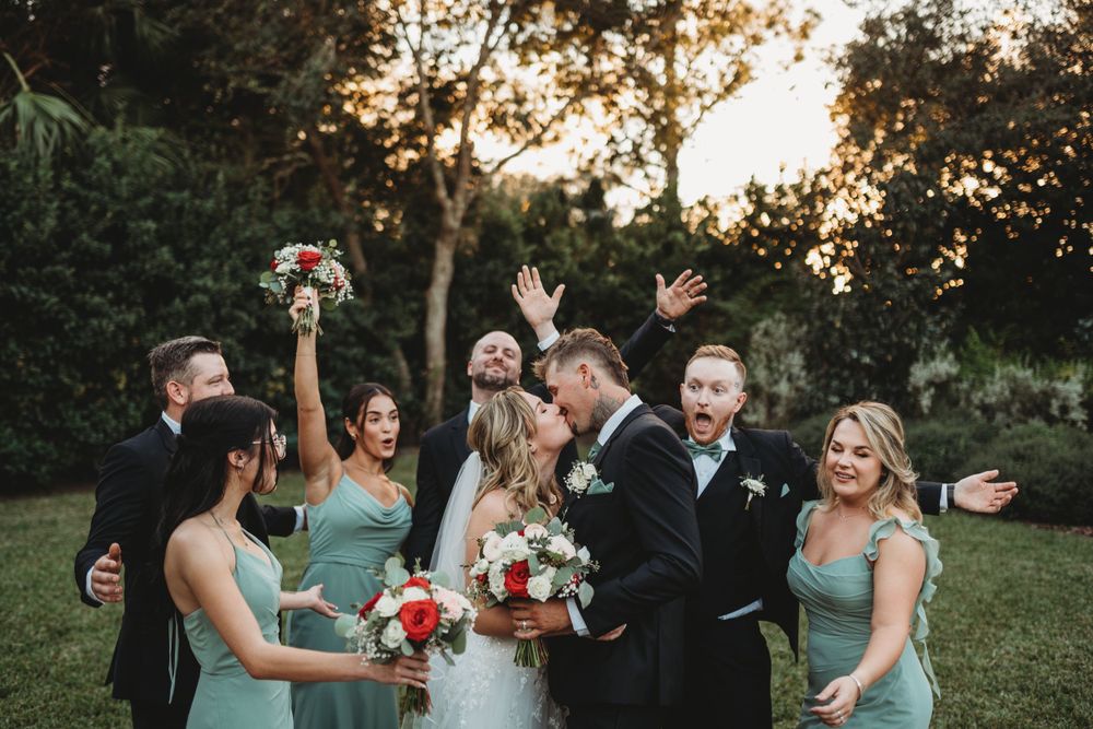 Joyful celebration with wedding party in mint green and black attire holding bouquets aloft.