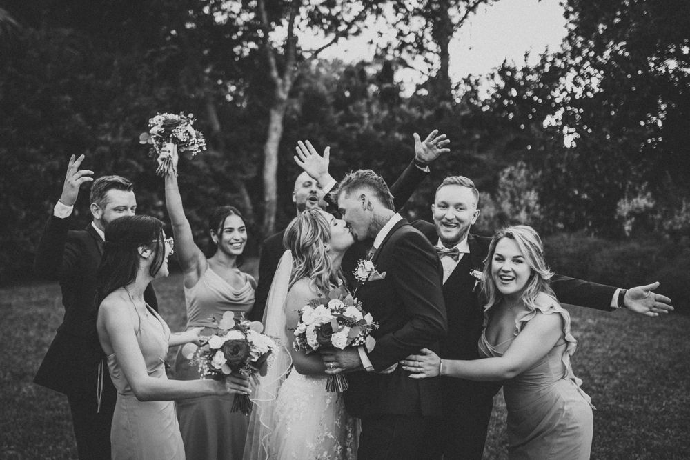 Joyful bridal party celebrating outdoors with raised arms and enthusiastic expressions.