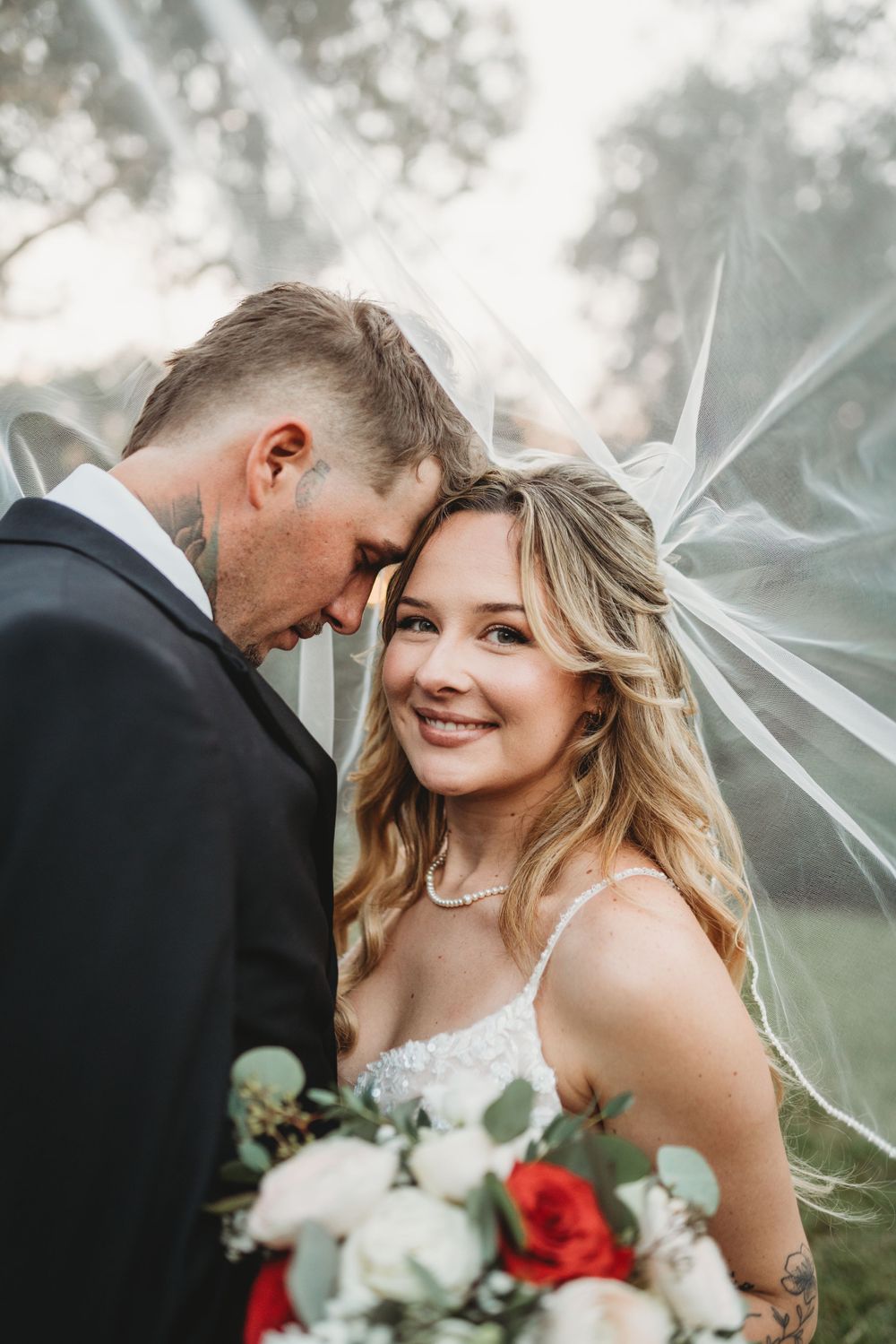 Romantic wedding portrait of couple sharing intimate moment under flowing veil.