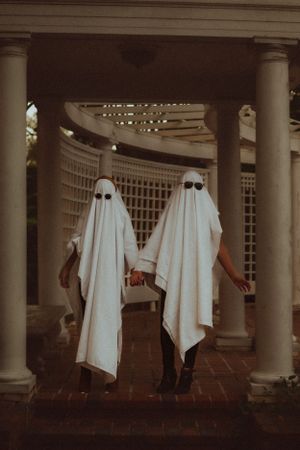 Two people dressed as playful ghosts pose in architectural archway.