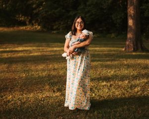 Mother holds newborn baby outdoors during golden hour photoshoot.