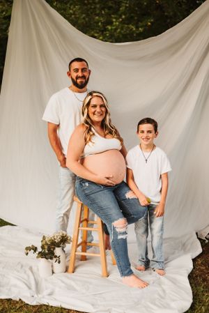 Family maternity photo against white backdrop outdoors with casual attire.