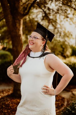 Graduate in white dress and cap smiling outdoors during commencement photoshoot.