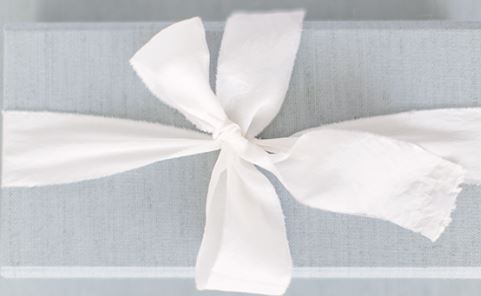 A delicate white ribbon bow tied against a soft gray background.
