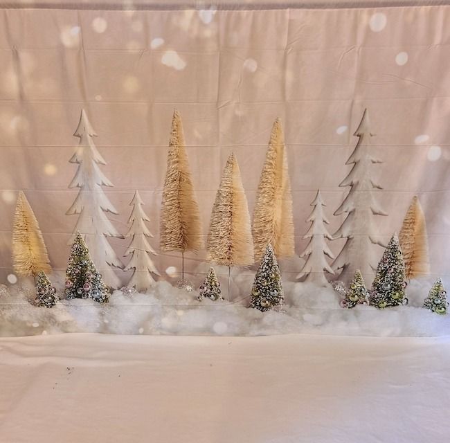 A winter wonderland scene with white and gold bottle brush trees on snowy fabric backdrop.