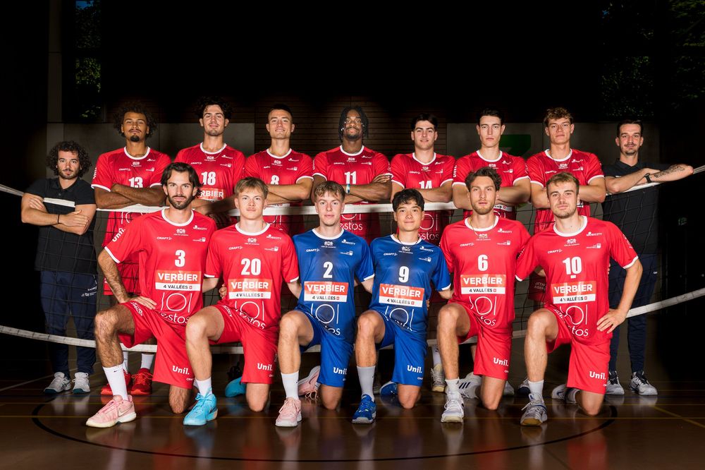 Soccer team members in red and blue uniforms sit together on a bench for a group photo.