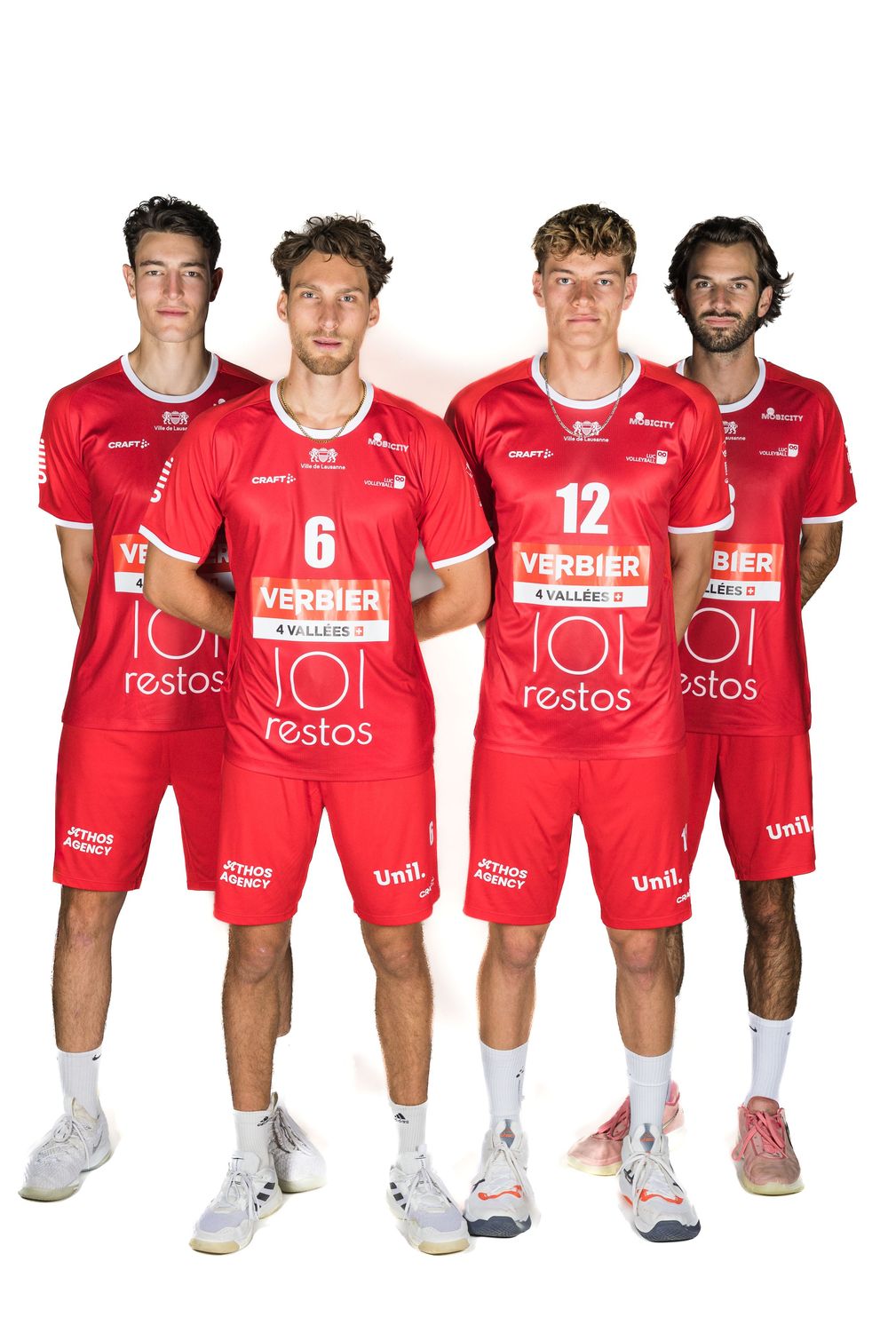 Sports team members in red uniforms with white text and logos crouch together for a team photo.