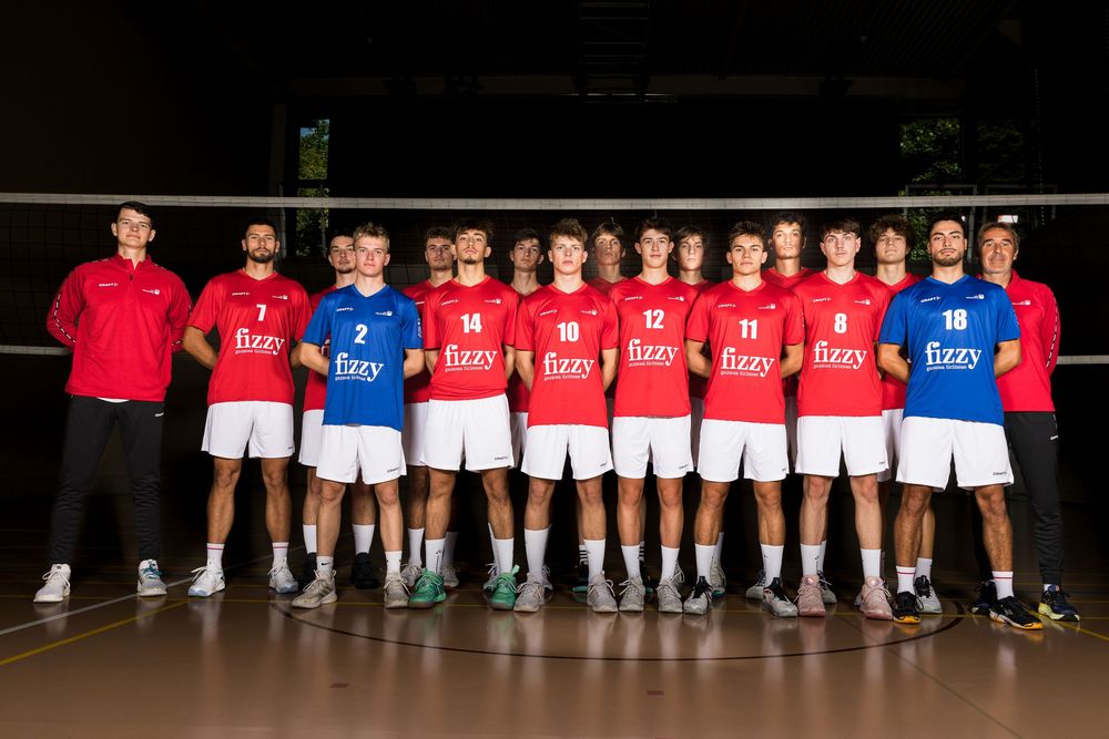 Group of volleyball players lined up in matching uniforms for a team photo on an indoor court.