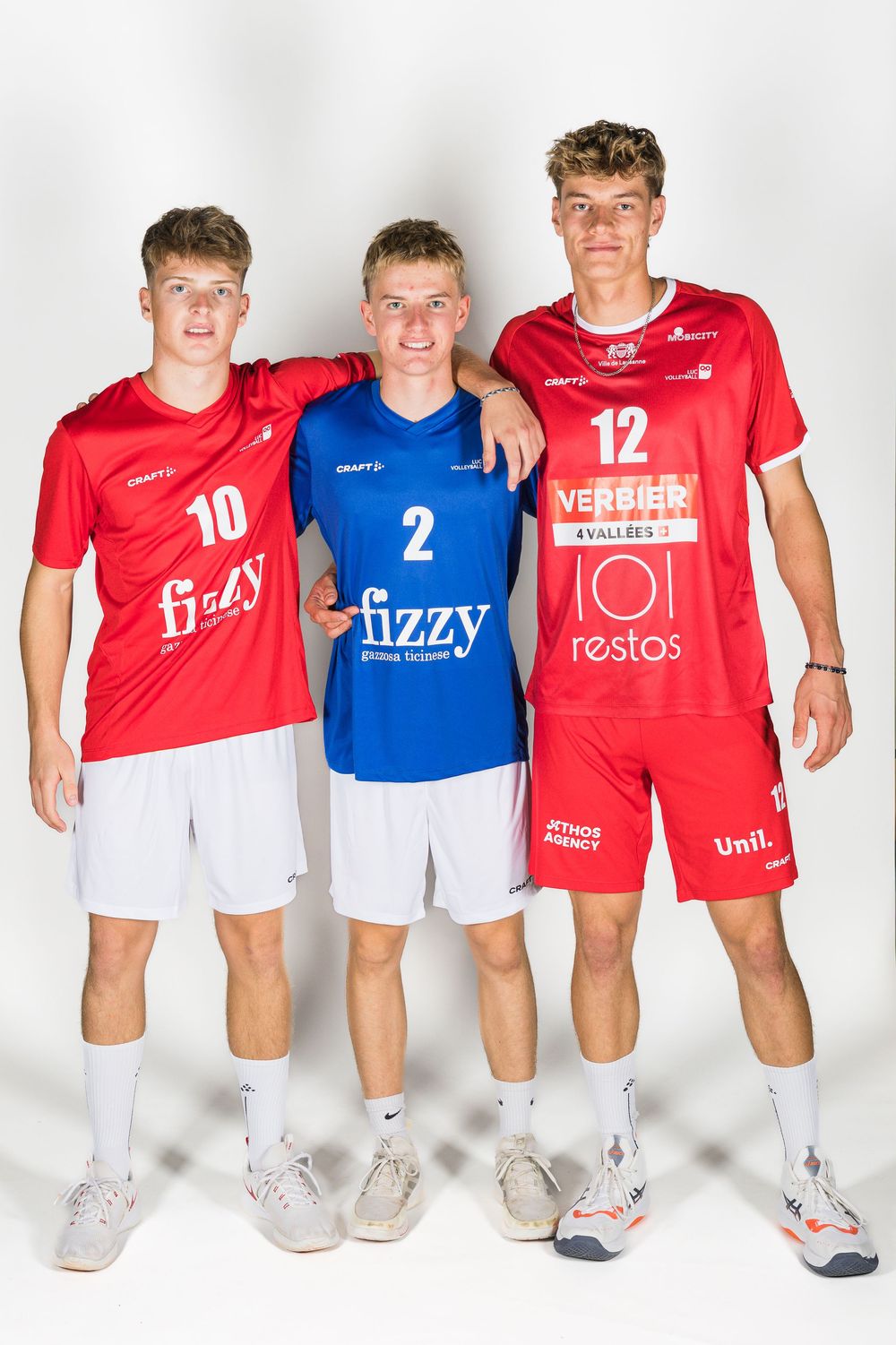 Group of athletes wearing red and blue sports uniforms with various sponsor logos standing together for team photo.