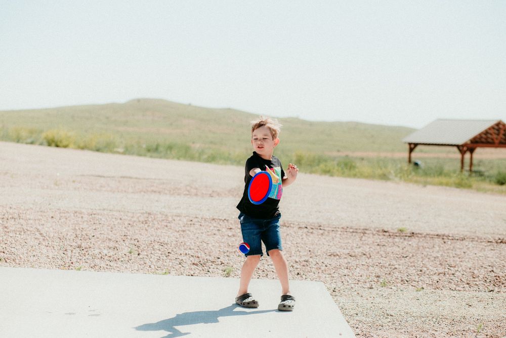 A figure stands in a rustic outdoor setting wearing a red and blue outfit at a dirt path junction.