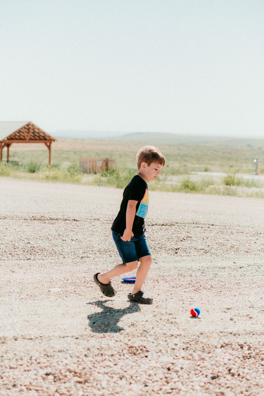 A person crouches down to play with a small red and white ball on a rocky desert terrain.