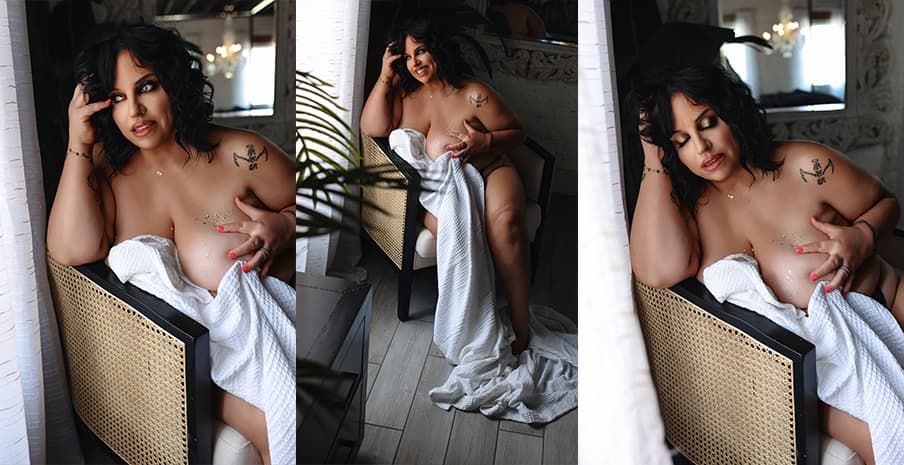 A figure draped in white fabric poses artistically in an elegant armchair against a light wall.