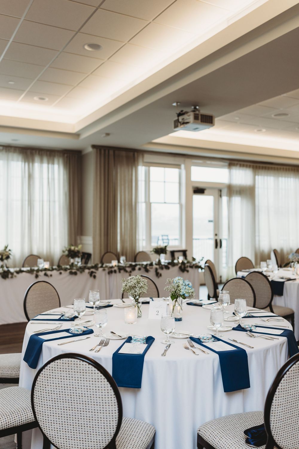 Round white dining tables decorated with navy blue napkins and elegant place settings in an upscale banquet room.