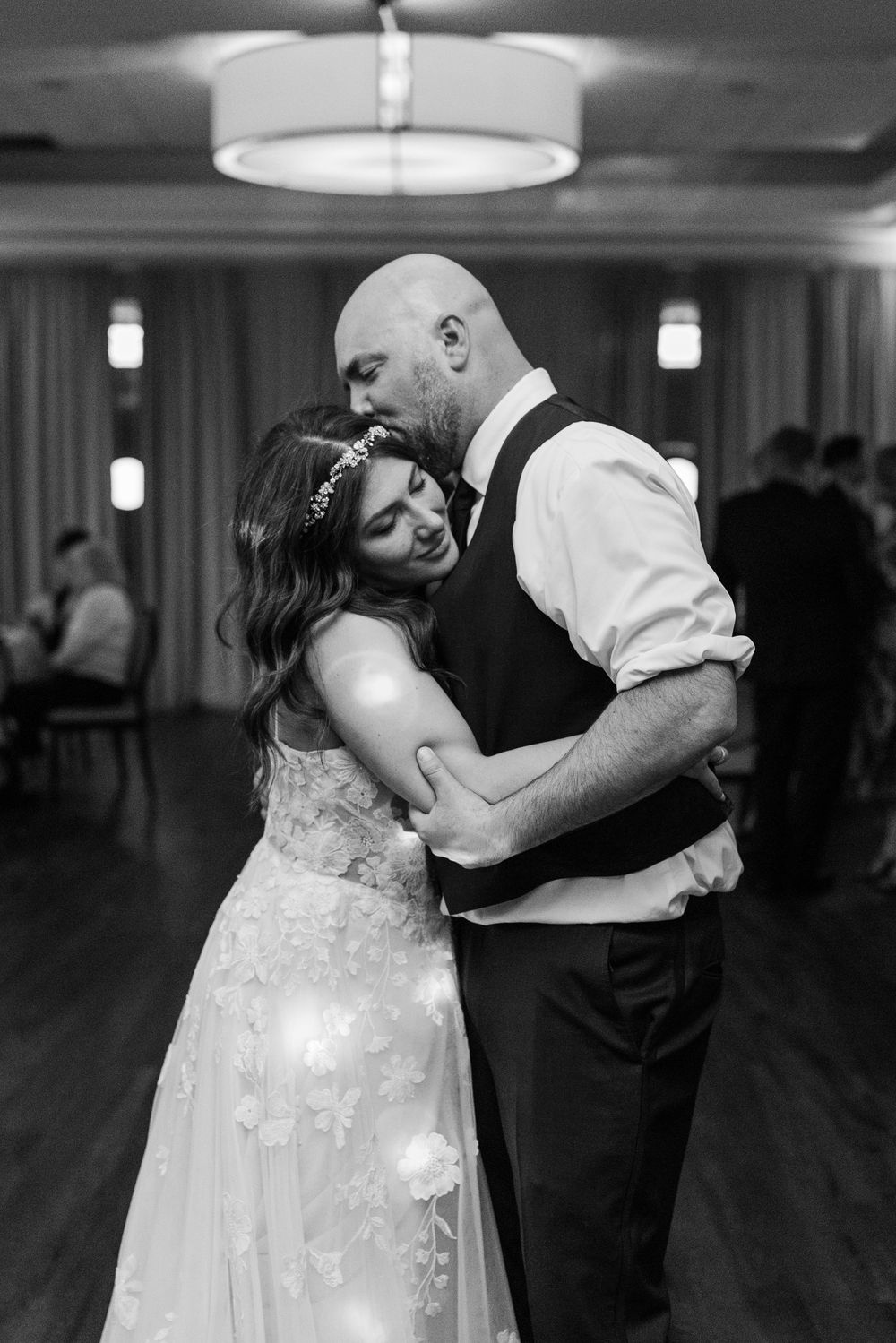 A tender black and white photograph of an intimate dance at a wedding reception with soft overhead lighting.
