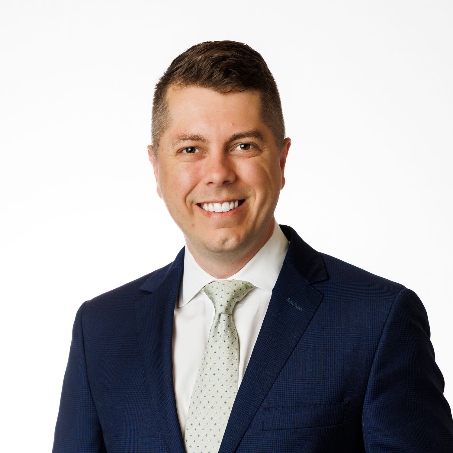Professional headshot of person in dark navy suit with light polka dot tie against white background.