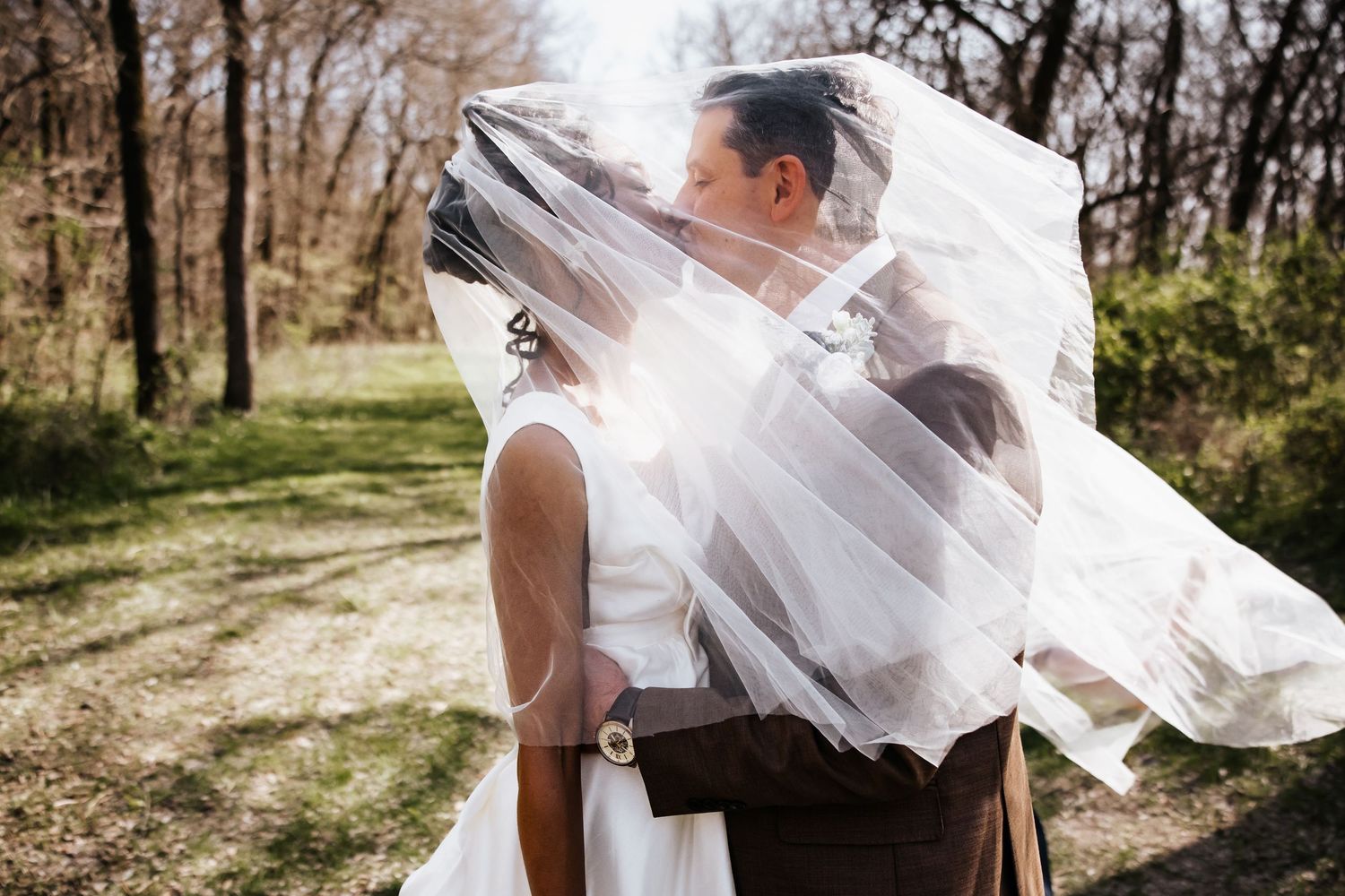 Bride and groom sharing a kiss hidden beneath a flowing white wedding veil.