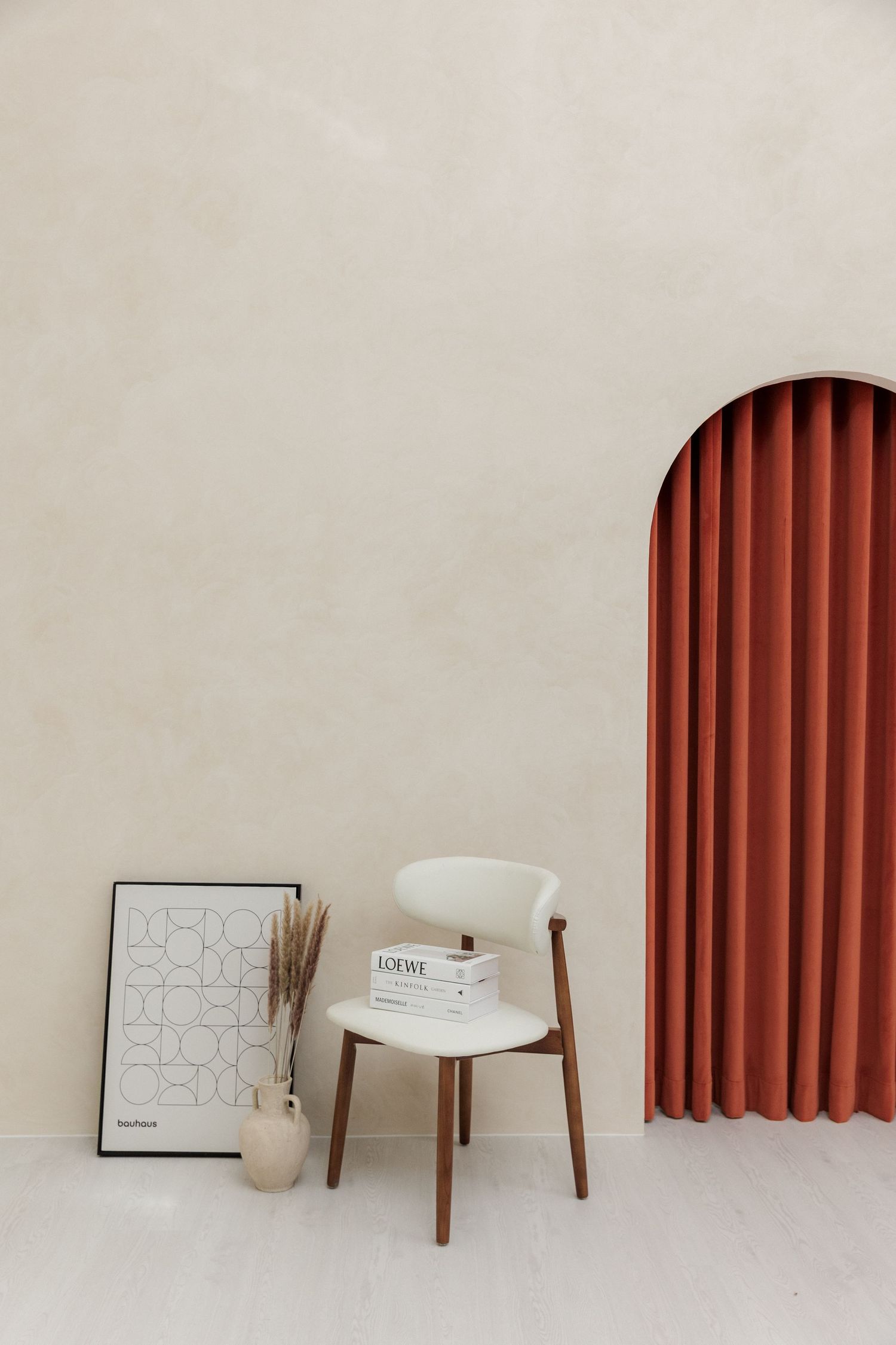 Minimalist interior scene with red curtains, white chair and framed artwork.