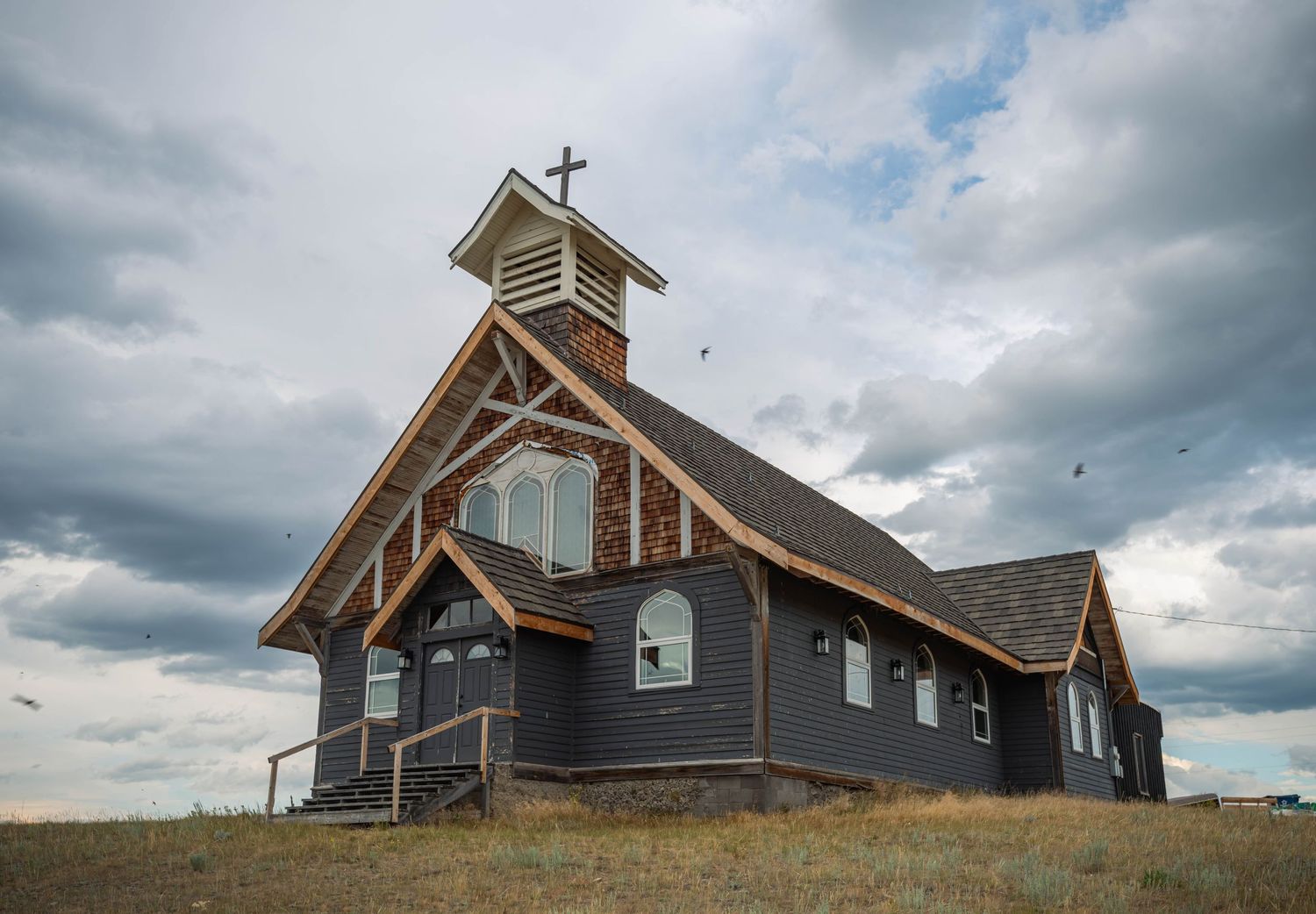 Ringling Church in Ringling, MT with a cross steeple stands on a hill under dramatic cloudy skies.