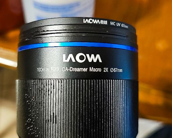 Close-up detail of a Laowa macro photography lens showing the blue and white branding against black lens barrel.
