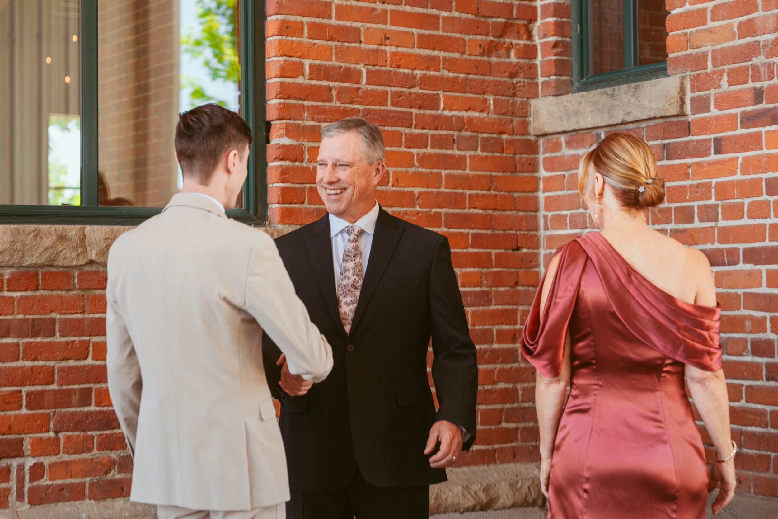 Wedding couple greets officiant outside brick church before ceremony.