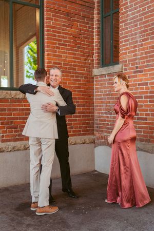 Wedding guests share warm embraces outside a historic brick building.