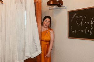 Person in an orange dress standing near white curtains and a chalkboard sign.