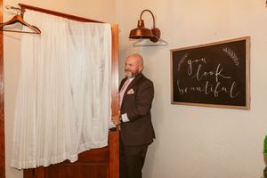 A wedding gown hangs elegantly against a window with rustic decor and chalkboard signs.
