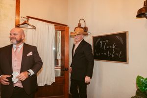 Groomsmen in formal attire share laughs in a rustic indoor venue with brick walls.
