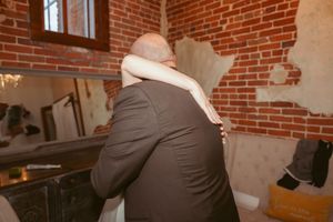 Emotional embrace captured from behind in a rustic brick-walled venue.