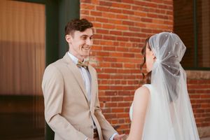 Two figures share a joyful moment in front of a rustic brick wall during a wedding ceremony.