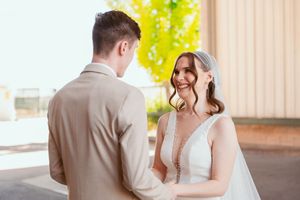 A couple shares a first look moment against a sunlit brick backdrop during their wedding day.