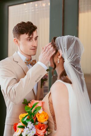 A tender wedding moment with the couple holding a vibrant orange and yellow bouquet together.