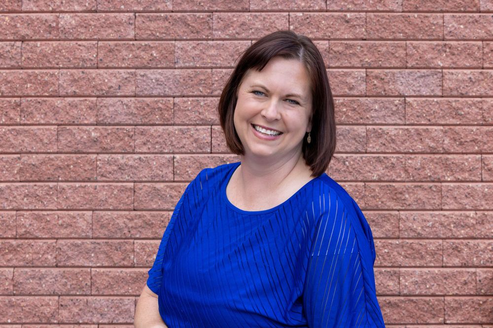 Person in royal blue top poses against brick wall texture background.