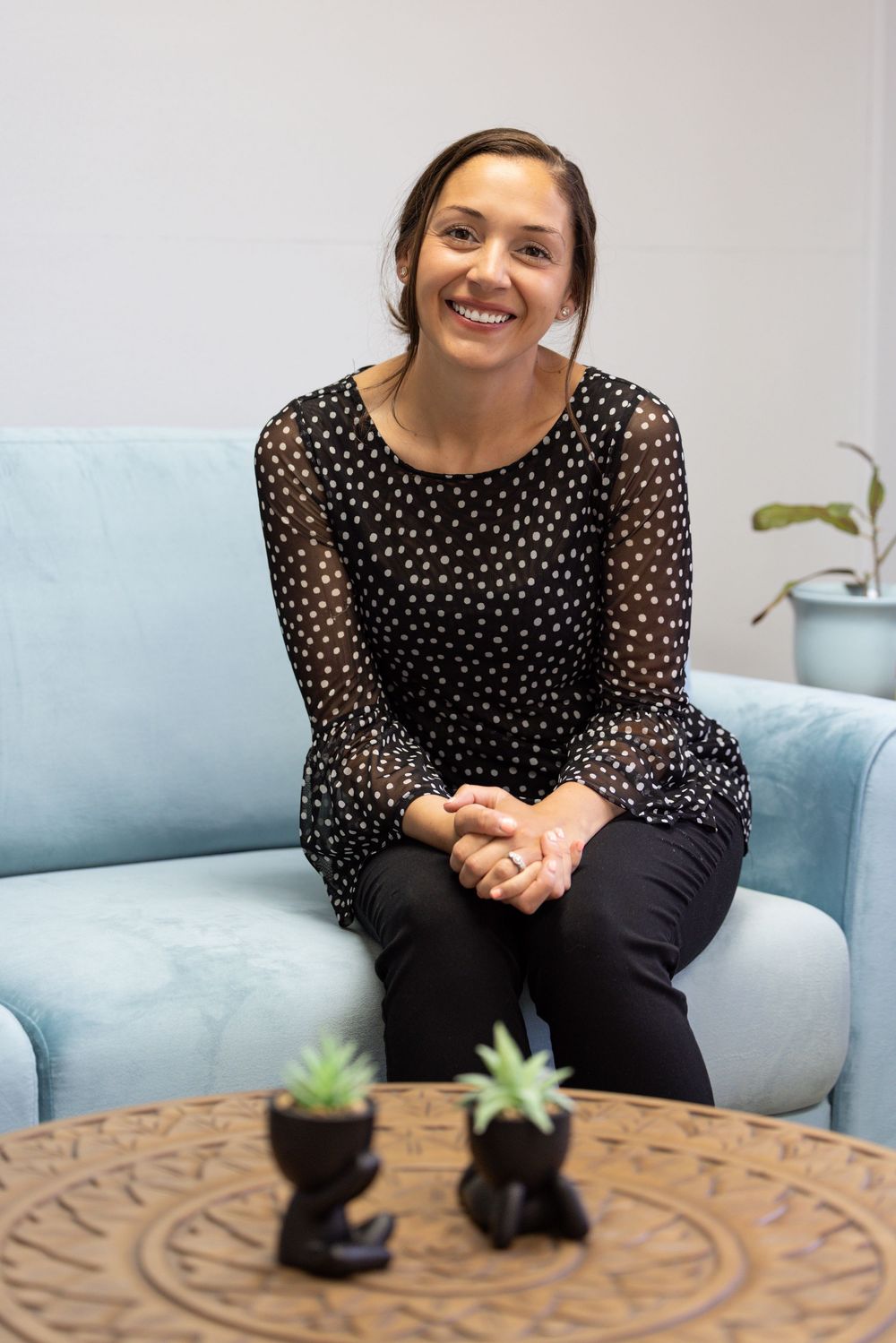 Someone wearing a polka dot top sits casually on a gray couch next to potted succulents on a wooden coffee table.